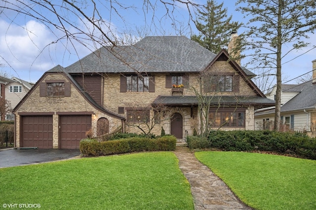 view of front facade featuring roof with shingles, aphalt driveway, a front lawn, and a chimney