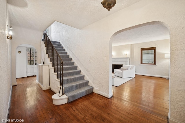 stairway featuring arched walkways, a textured wall, and wood-type flooring