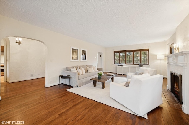 living room with arched walkways, a lit fireplace, a textured ceiling, and wood finished floors