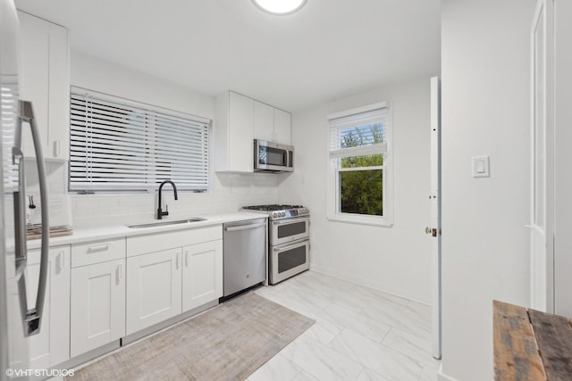 kitchen featuring marble finish floor, tasteful backsplash, appliances with stainless steel finishes, white cabinetry, and a sink