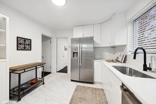 kitchen featuring stainless steel appliances, a sink, white cabinets, marble finish floor, and light countertops