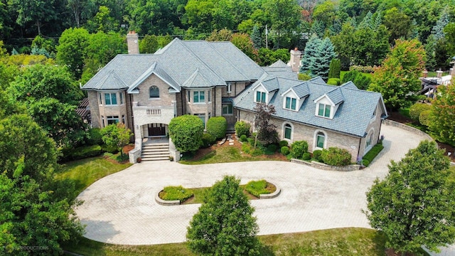 view of front of house with driveway, stone siding, a chimney, and a high end roof