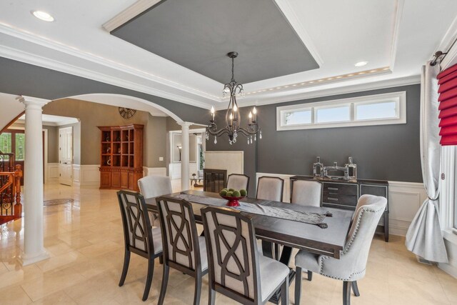 dining area featuring decorative columns, arched walkways, a raised ceiling, a wainscoted wall, and a decorative wall