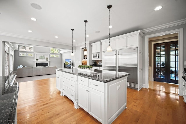 kitchen featuring built in appliances, light wood finished floors, a fireplace, and crown molding