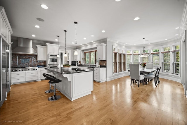 kitchen with wall chimney range hood, backsplash, appliances with stainless steel finishes, and white cabinetry