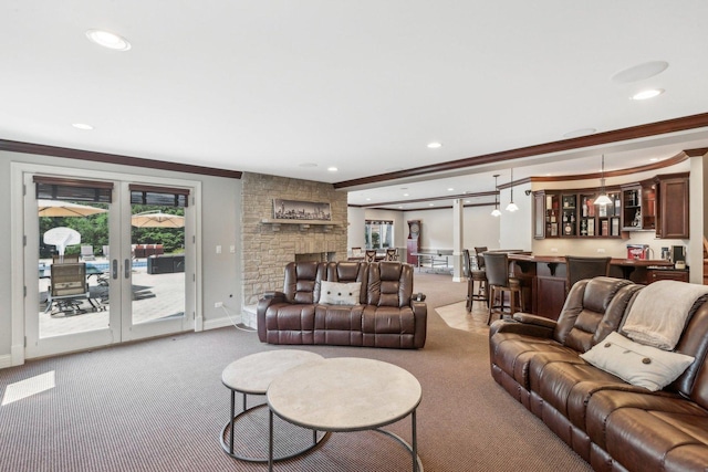 carpeted living room featuring baseboards, wet bar, ornamental molding, and a stone fireplace