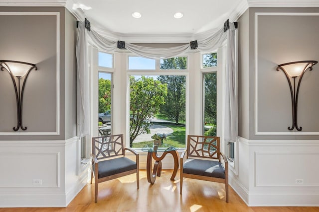 sitting room featuring light wood-type flooring, ornamental molding, and a decorative wall