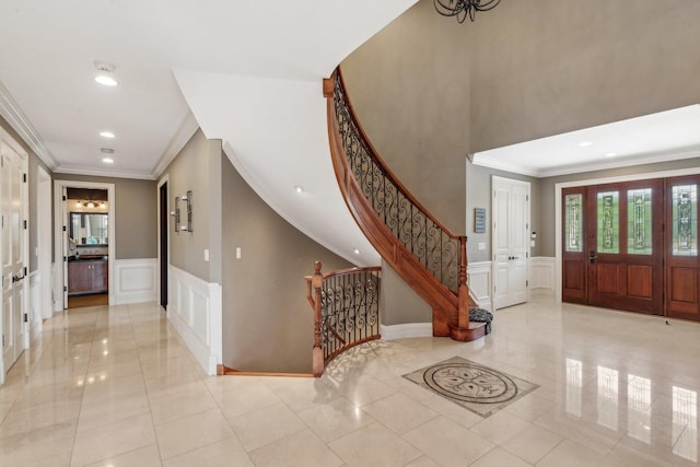 foyer entrance featuring a wainscoted wall, ornamental molding, stairs, a decorative wall, and recessed lighting