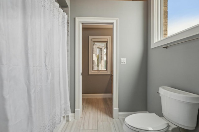 bathroom featuring a shower with curtain, toilet, and baseboards