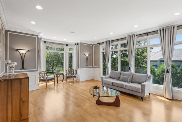 living area featuring crown molding, plenty of natural light, a decorative wall, and light wood finished floors