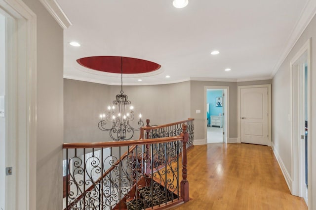 corridor featuring light wood finished floors, baseboards, crown molding, an upstairs landing, and a chandelier