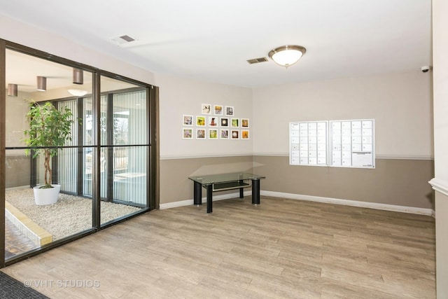 interior space with mail area, wood finished floors, visible vents, and baseboards