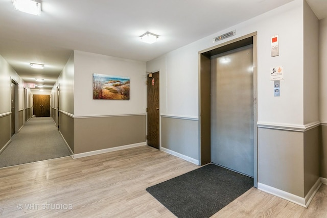 hall featuring elevator, wood finished floors, and baseboards