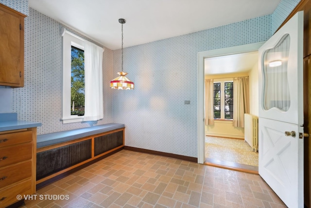 unfurnished dining area featuring baseboards, brick patterned floor, radiator heating unit, and wallpapered walls