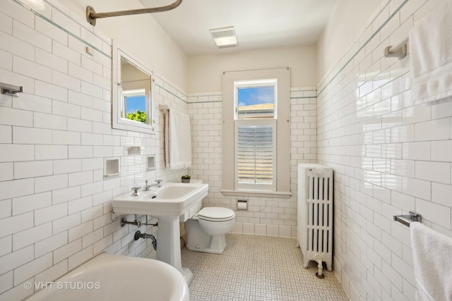 full bath with tile patterned floors, toilet, a tub, radiator, and tile walls