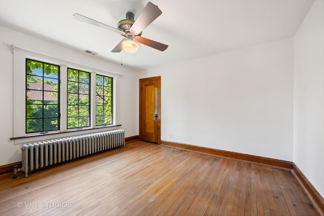 spare room with visible vents, light wood-style flooring, radiator, baseboards, and ceiling fan