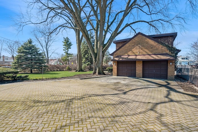 view of side of home with decorative driveway, brick siding, a garage, and fence