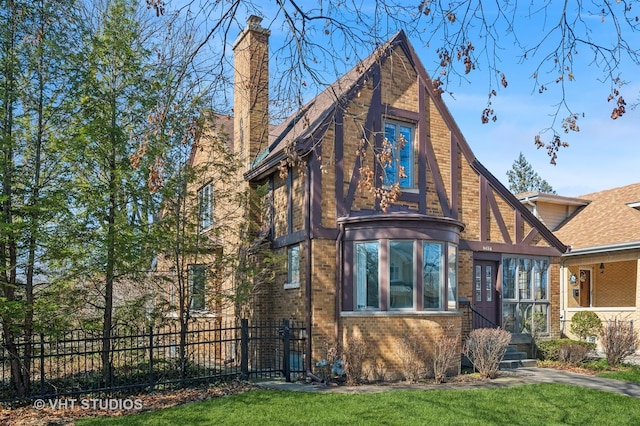 tudor home with a front yard, brick siding, a fenced front yard, and a chimney