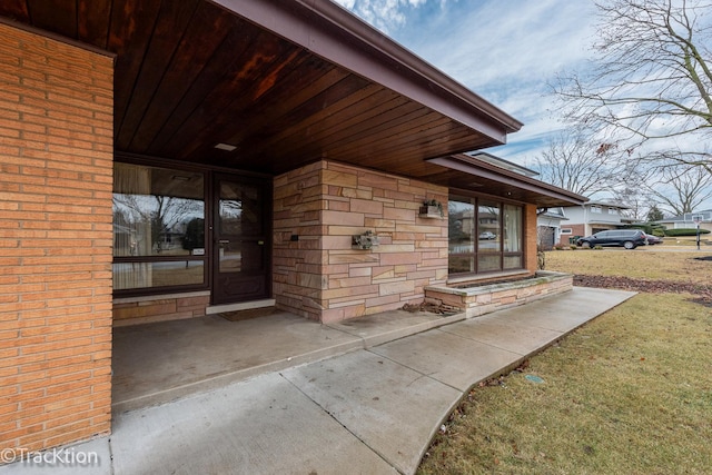 view of exterior entry with stone siding and a lawn