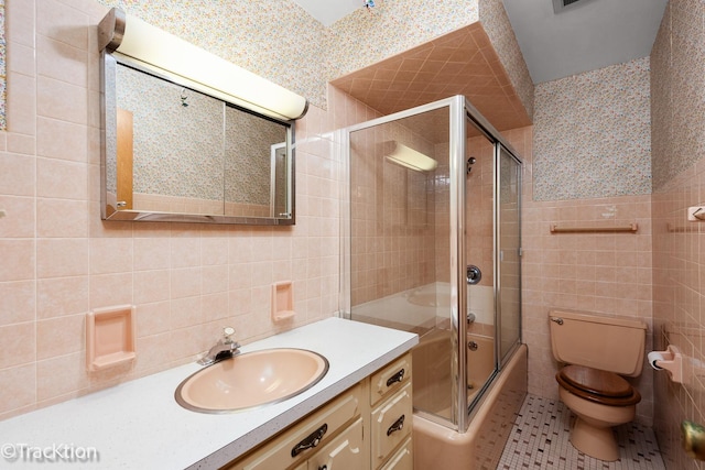 bathroom featuring toilet, tile patterned flooring, combined bath / shower with glass door, vanity, and tile walls