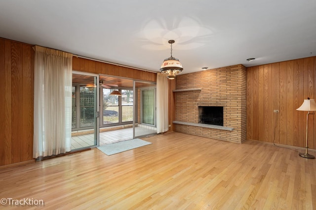 unfurnished living room with wood walls, a brick fireplace, and light wood-style floors