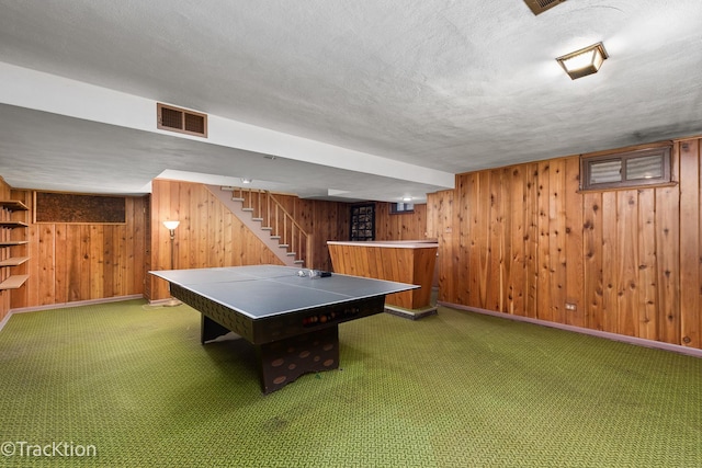 recreation room featuring wooden walls, a textured ceiling, visible vents, and carpet flooring