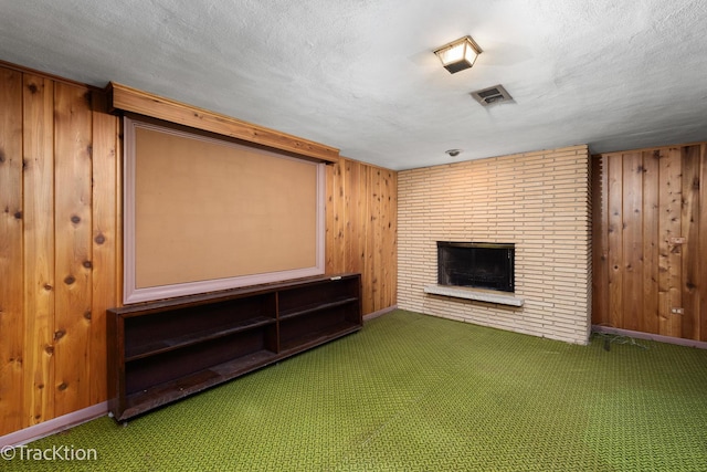 unfurnished living room with carpet floors, a fireplace, visible vents, wood walls, and a textured ceiling