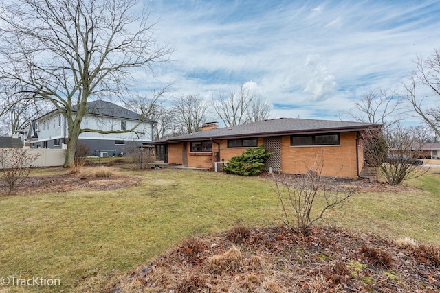 rear view of house with brick siding, a yard, a chimney, fence, and cooling unit