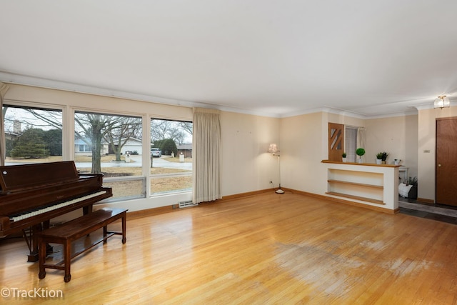 living area featuring baseboards, light wood finished floors, and crown molding