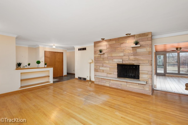 unfurnished living room featuring visible vents, crown molding, a stone fireplace, and wood finished floors