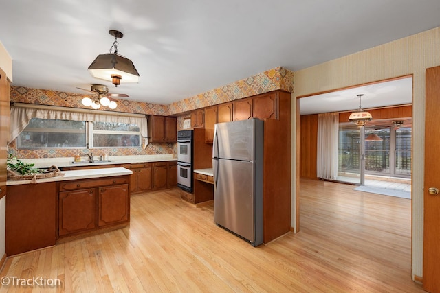 kitchen with stainless steel appliances, brown cabinetry, light countertops, and light wood-style floors