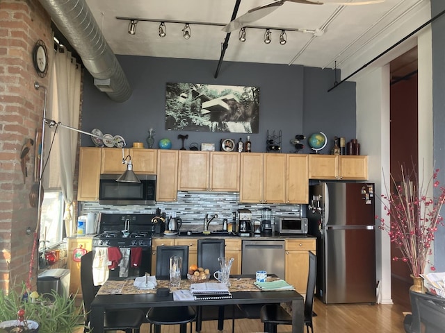 kitchen with light brown cabinets, light wood-style floors, appliances with stainless steel finishes, decorative backsplash, and dark countertops