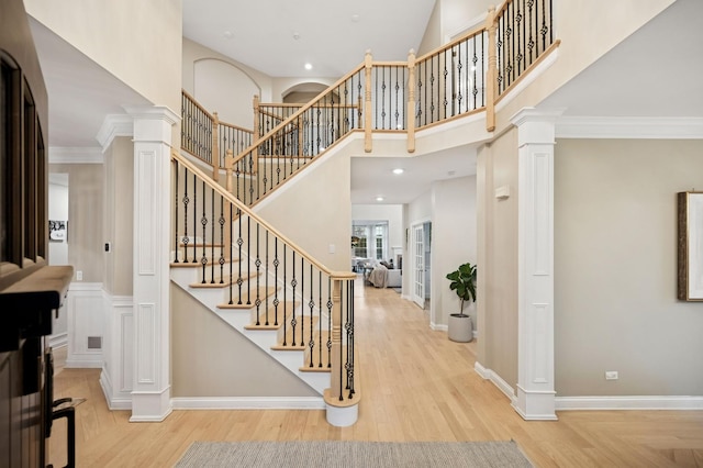 entrance foyer featuring wood finished floors, a high ceiling, crown molding, decorative columns, and baseboards