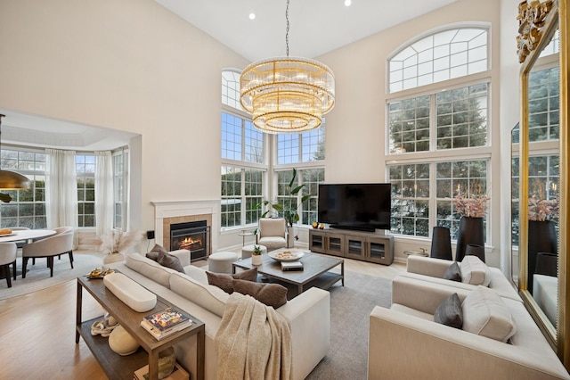 living room featuring wood finished floors, an inviting chandelier, recessed lighting, a towering ceiling, and a tiled fireplace