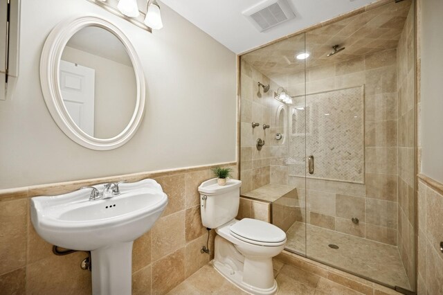 bathroom with a wainscoted wall, visible vents, a shower stall, tile walls, and toilet