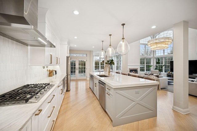 kitchen with a sink, stainless steel appliances, white cabinets, a fireplace, and wall chimney range hood