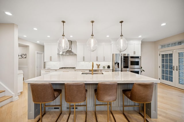 kitchen featuring wall chimney range hood, decorative backsplash, appliances with stainless steel finishes, french doors, and a sink