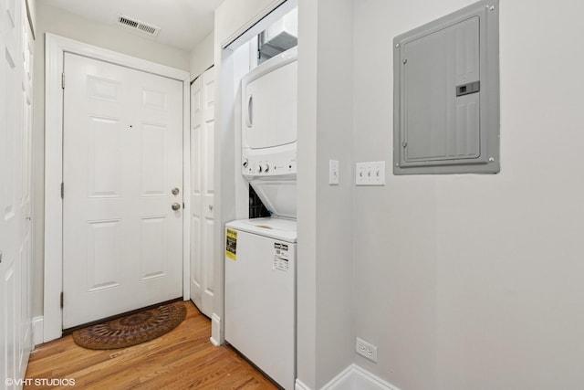 laundry room featuring laundry area, stacked washing maching and dryer, light wood-type flooring, visible vents, and electric panel