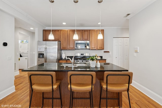 kitchen with visible vents, a center island with sink, a sink, stacked washer and clothes dryer, and stainless steel appliances