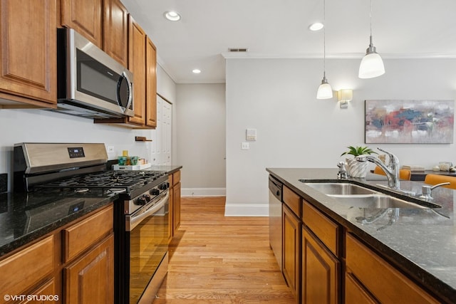 kitchen with a sink, light wood finished floors, stainless steel appliances, baseboards, and ornamental molding