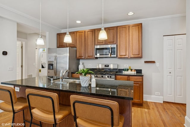 kitchen featuring brown cabinets, appliances with stainless steel finishes, a sink, light wood-type flooring, and a kitchen bar