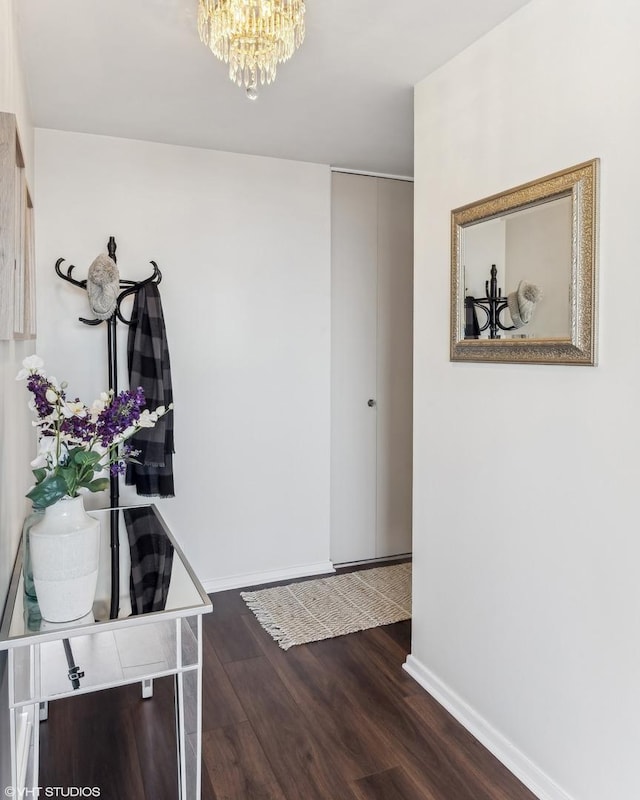 hall featuring baseboards, an inviting chandelier, and wood finished floors