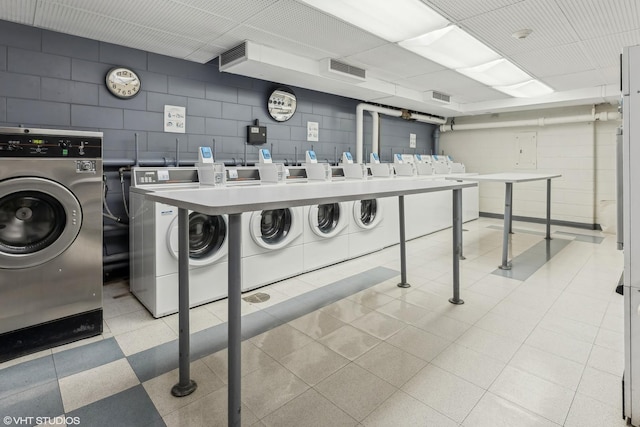 common laundry area with washer and clothes dryer, visible vents, and concrete block wall