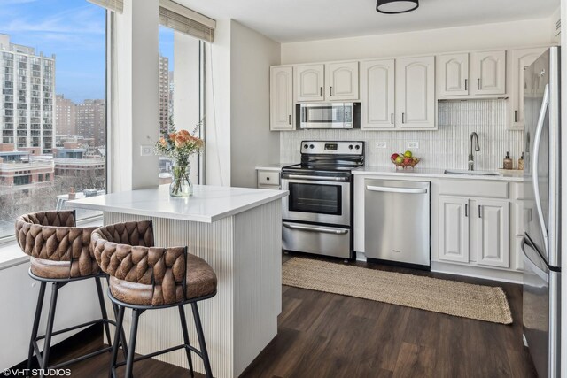 kitchen with a breakfast bar, a sink, backsplash, dark wood finished floors, and appliances with stainless steel finishes