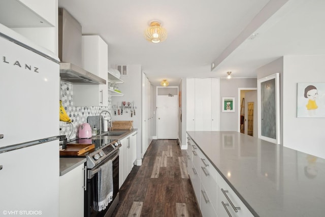 kitchen with a sink, white cabinets, wall chimney range hood, stainless steel electric range, and freestanding refrigerator