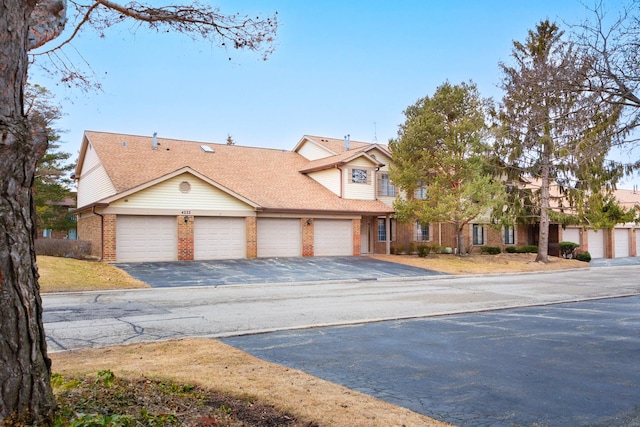 view of front of home with driveway, an attached garage, a shingled roof, and brick siding