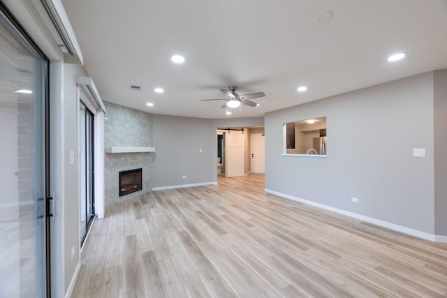 unfurnished living room with recessed lighting, visible vents, a barn door, light wood-type flooring, and baseboards