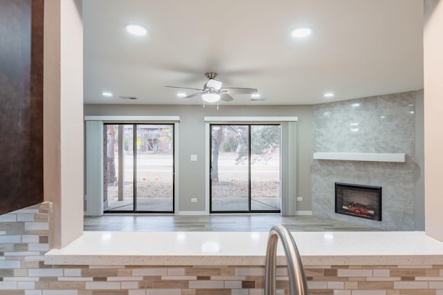 kitchen featuring stone counters, recessed lighting, wood finished floors, a ceiling fan, and a tiled fireplace