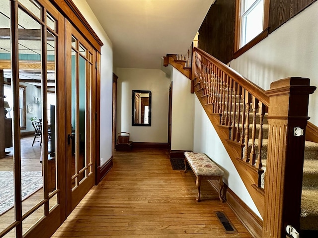 corridor featuring stairs, hardwood / wood-style flooring, visible vents, and baseboards