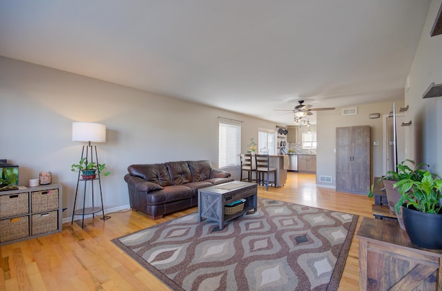 living room with visible vents, baseboards, light wood-style floors, and a ceiling fan